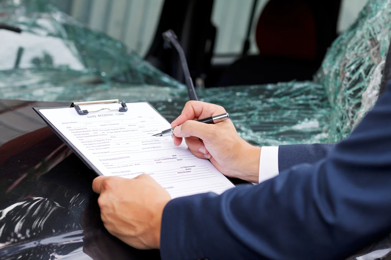 Driver signing important claim paperwork beside a wrecked car, showing how Clay Travis Law helps Southerners after a crash turns life upside down.